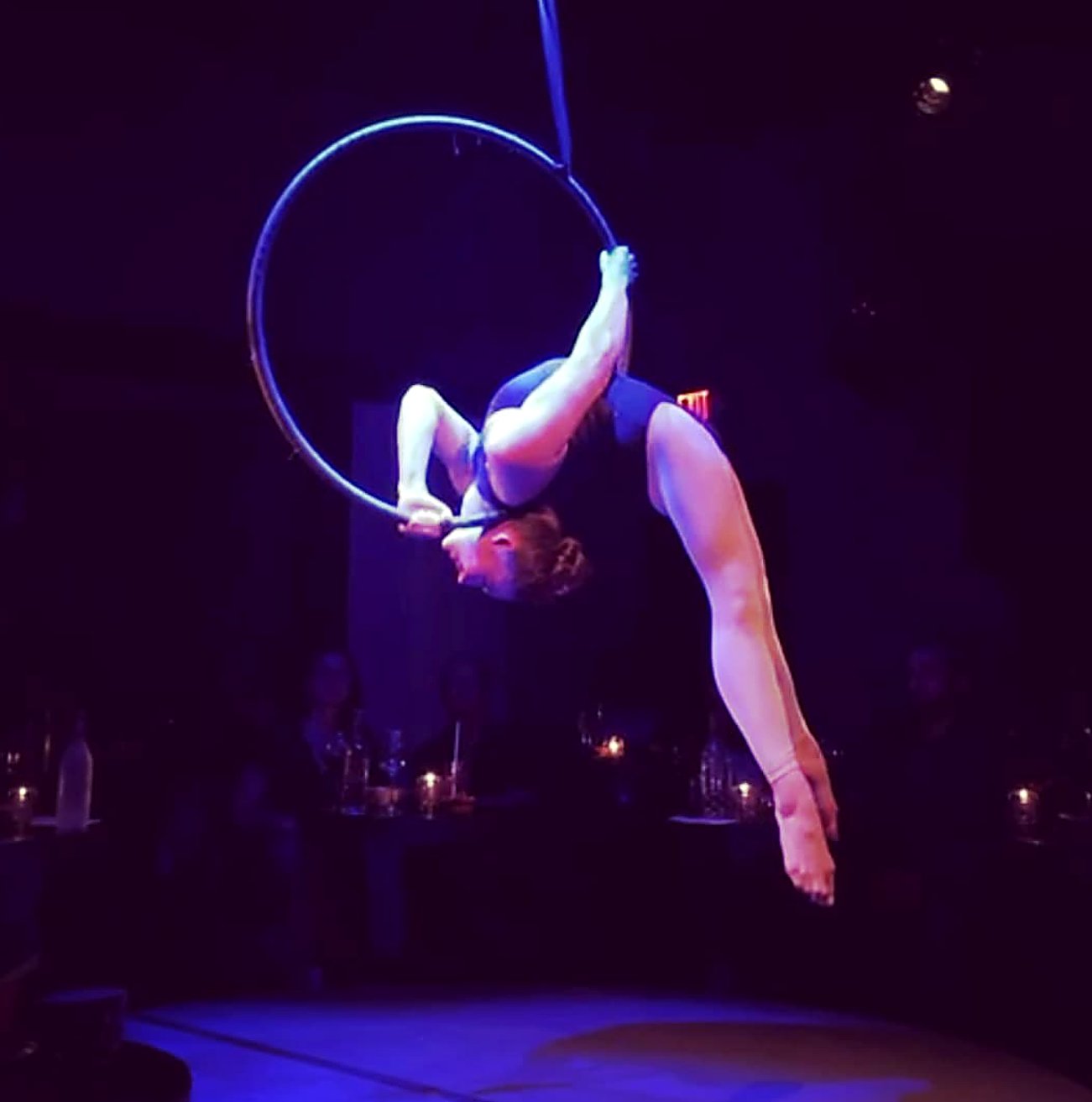 Aerial hoop performance in a candlelit venue under purple light